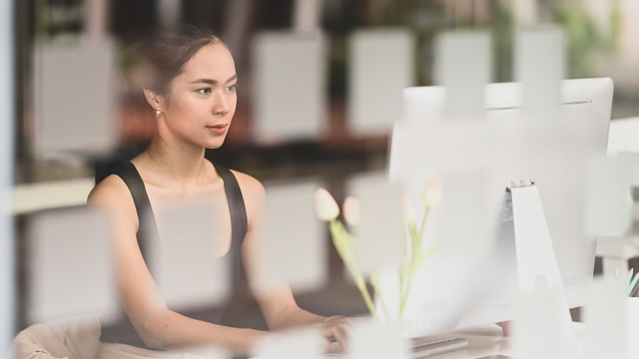 Frau vor Bildschirm hinter Fenster.